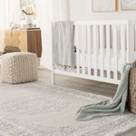 Closer view of rug with white crib, gray and green throws, knitted pouf, and wooden side table