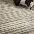 Close-up of Humphrey Natural Moss Rug's soft texture and striped pattern next to a cream armchair and black side table