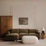 Room view of Marion Square Ottoman placed on light rug with green sectional sofa and side table