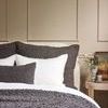 dark gray Murphy Pillow styled on bed with white linens and neutral wall paneling