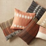 Group of assorted tribal patterned pillows including black/ivory, brick red, and beige color variations on textured surface