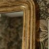 Close-up of mirror's top left corner with textured gold frame against floral wallpaper backdrop
