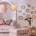Cluster of decorative plates mounted on baby pink button spot wallpaper in a living room corner
