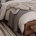 Close-up of rug visible under knitted throw and layered bedding on rattan bed.