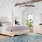 Bedroom scene with bed, matching dresser with mirror, white chair, and decorative plants in bright room