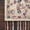 Close-up of rug corner on dark wood floor showcasing floral motifs and braided tassels in soft pastel colors