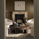 Round coffee table styled in living room with beige chairs, decorative vases, and patterned rug
