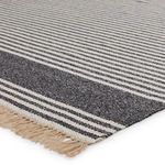 Close-up angled view showing texture and fringed edge of dark gray and beige striped rug