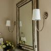 Pair of sconces flanking a large beveled mirror above marble countertop and silver faucet