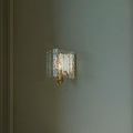 Wall mounted Duvernell Sconce glowing warmly with overlapping textured recycled glass sheets