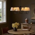 Larson Chandelier illuminated and hanging over round dining table in warm toned dining room with window and artwork