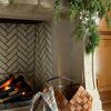 Plaid throw draped over a basket in front of a stone fireplace with greenery decorating the mantel