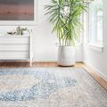 Layla rug angled on hardwood floor in bright white room with green potted plant and dresser in background