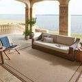 Merrick Chestnut Oatmeal Rug styled on covered outdoor patio with wicker sofa and lake view
