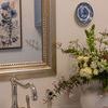 Painting visible in reflection above kitchen sink with silver faucet and floral arrangement