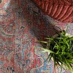 Close-up of rug texture under folded corner of dark red corduroy pouf and green plant in tan pot