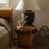 Pecola lamp styled in a bedroom setting on a rustic wooden stool next to bed and woven basket