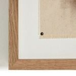 Close-up of canvas corner pinned with brass tacks inside natural wood frame