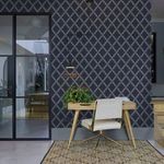 Greenskeeper Wallpaper applied on wall in a styled room featuring wood desk, chair, hanging lamp, and glass door