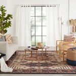 Living area showing rug beneath knit pouf and wood armchairs near large window