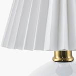 Detailed close-up of white pleated linen lamp shade atop brass lamp neck