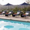 Row of chaises by poolside with blue and white patterned cushions, orange towels, and blue umbrellas