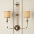 Wall sconce with lit fabric drum lampshades casting warm light on beige paneled wall