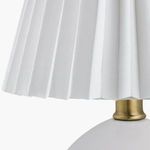 Detail of pleated white linen lamp shade and brass neck connection to ceramic base