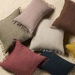 Overhead view of blush pink pillow among other colored linen pillows with tassels on textured rug