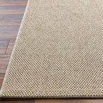 Close-up view of tightly woven beige and off-white fibers on rug surface with floor edge visible
