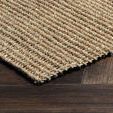 Close-up corner view of seagrass rug showing woven edge detail on dark wood flooring
