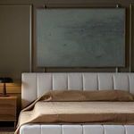 Painting hung on dark olive wall above beige tufted bed with warm brown bedding in modern bedroom setting
