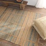 Close angled view of rug showing texture alongside stacked woven cushions near wood bench