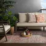 Outdoor seating area with rug beneath a sofa and chair, surrounded by green foliage and dark gray wall