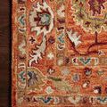 Macro view highlighting detailed wool hook texture and vibrant colors of the orange and buff floral pattern on wooden floor