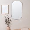 Mirror mounted on beige wall above wooden bench with drying towel and decorative vase