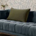 olive green pillow displayed on a deep blue tufted sofa with floral wallpaper background
