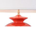 Close-up of lamp's glossy red ceramic neck under white shade with brass finial