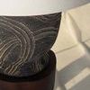 Side close-up showing lamp base resting on dark wooden stool with sunlit floor shadows