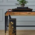 Close-up of umbrella stand with black umbrella featuring gold flower design beside desk with wooden drawers