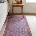 Rug placed under small wooden table beside bed on wood floor with light wall background