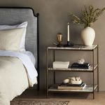 Nightstand styled in bedroom with bed and soft neutral-toned bedding in background