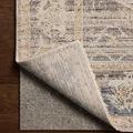 Milena rug corner lifted to reveal non-slip grey rug pad underneath on hardwood floor.