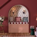 Arched alcove wallpapered with floral pattern, styled with striped and floral cushions on a pink bench with burgundy walls