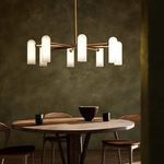 Odyssey Round MD Chandelier lit, hanging above round wood dining table with chairs and ceramic decor