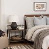 Bedroom with rug under nightstand holding table lamp with beige and gray pillows on bed.