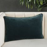 Teal lumbar pillow styled on cream tufted sofa with greenery in background