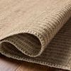 Close-up of rug partially rolled on wooden floor highlighting woven wool and cotton texture