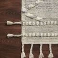 Detailed view of rug corner on wood floor highlighting linear braided pattern and tassels