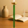 Glass candle holder lit with a candle, placed on wooden surface with blurred background of book and vase